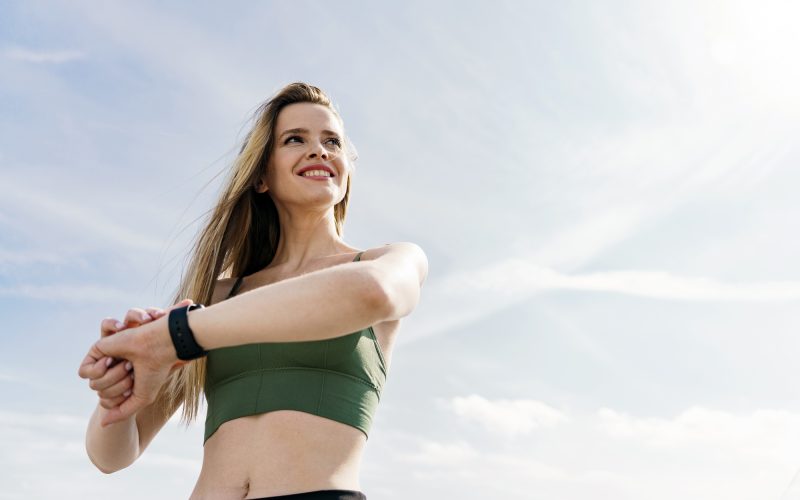 strong woman uses a fitness watch for sports training. The athlete smiles portrait against the sky.